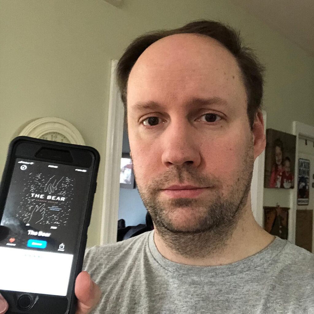 Matt holding up a phone with an audiobook of "The Bear"